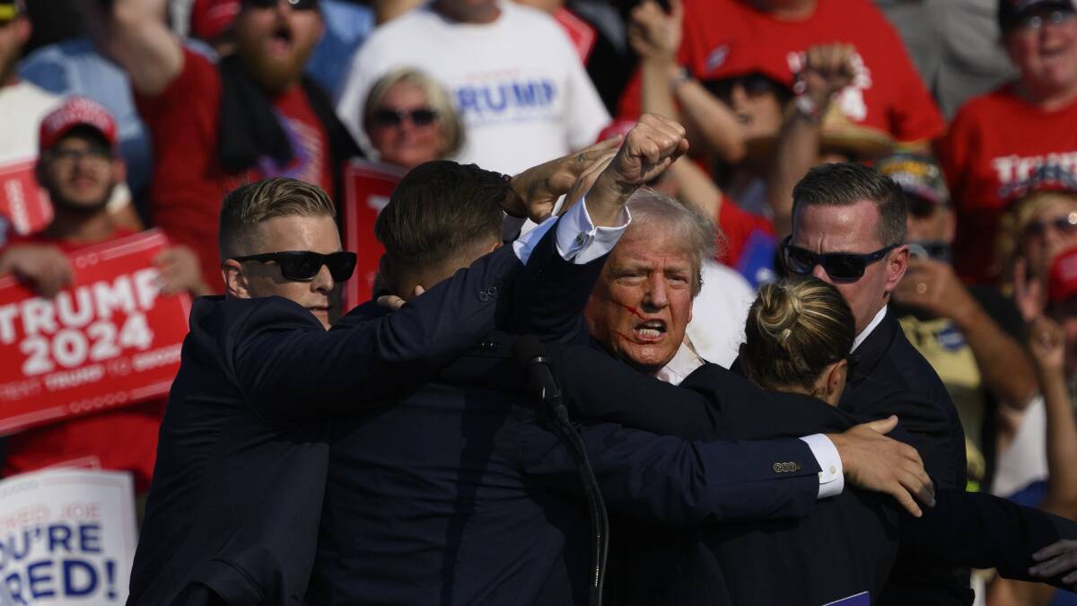 Donald Trump raises his fist in the air while being escorted away by Secret Service agents. Picture Getty Images