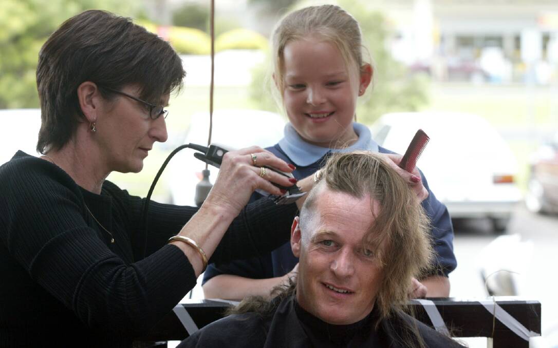 Warrnambool dentist Mike Johns having his long hair shaved off by Men Only hairdresser Debbie Jones and Sharna Jenkins, 9, at a Mitre 10 fundraising event.